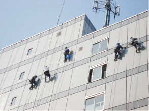 5人のスタッフが屋上からクライミングをしながらシーリング作業をしているところ